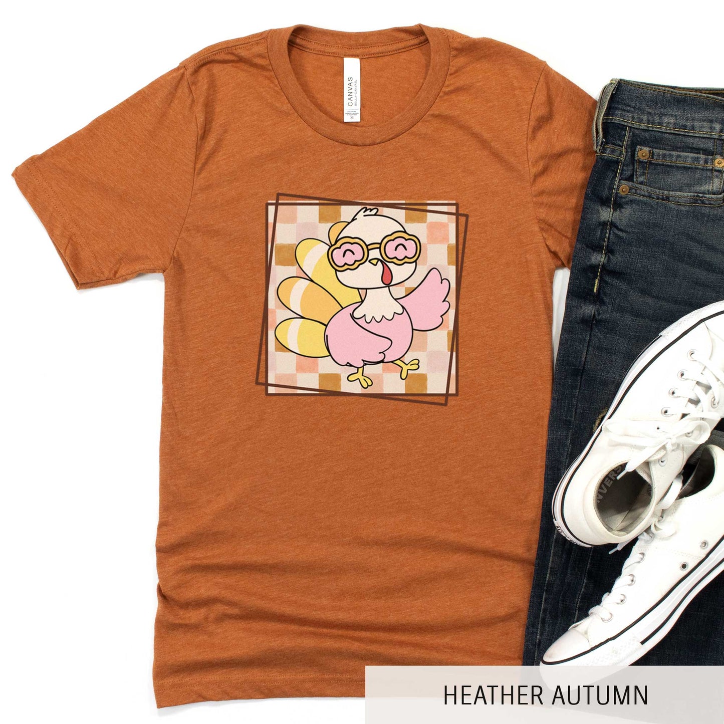 A heather autumn Bella Canvas t-shirt featuring a cute cartoon turkey against a fall checkered background.
