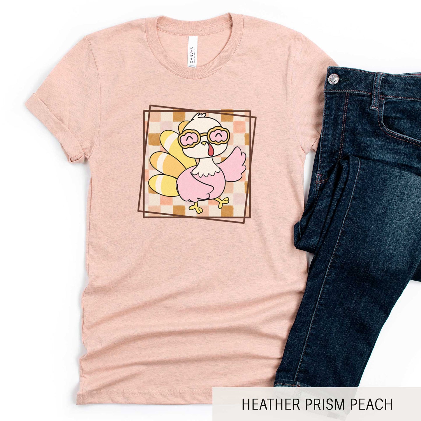 A heather prism peach Bella Canvas t-shirt featuring a cute cartoon turkey against a fall checkered background.