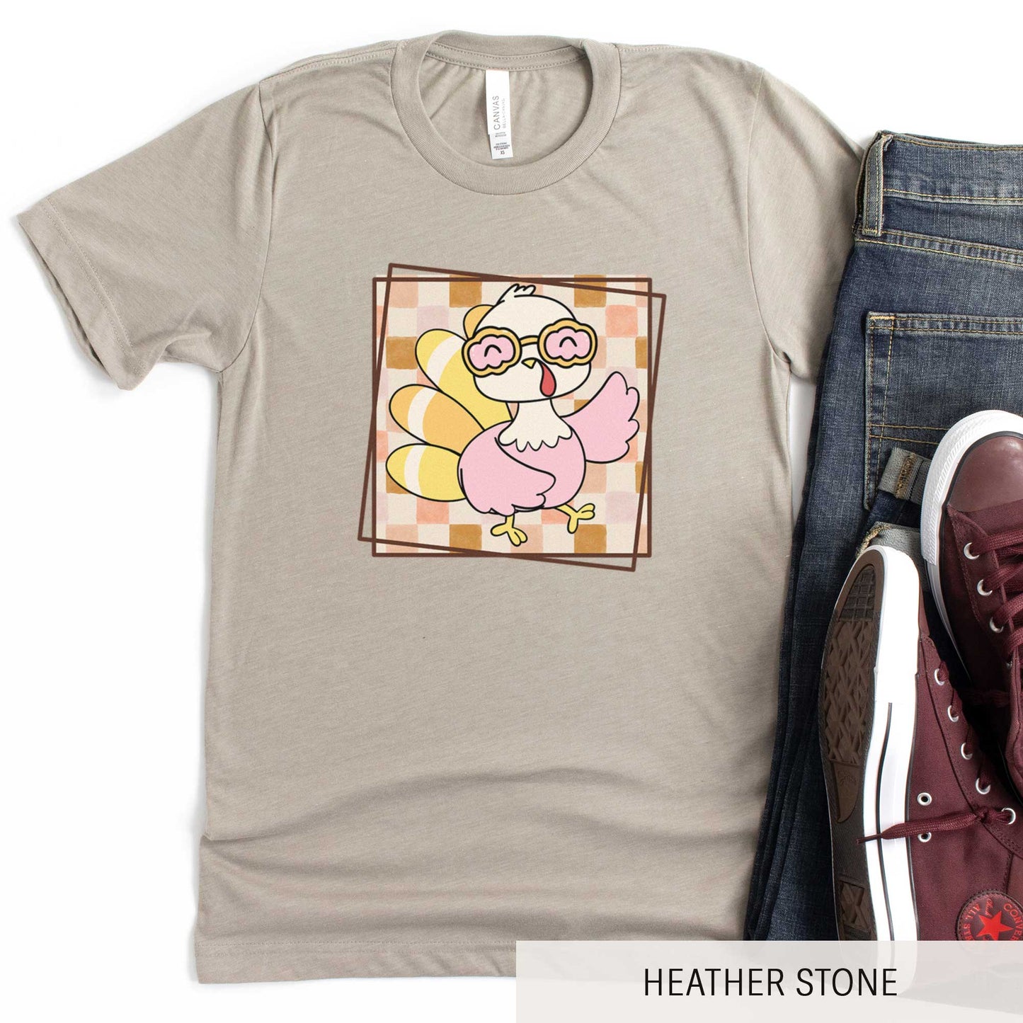 A heather stone Bella Canvas t-shirt featuring a cute cartoon turkey against a fall checkered background.