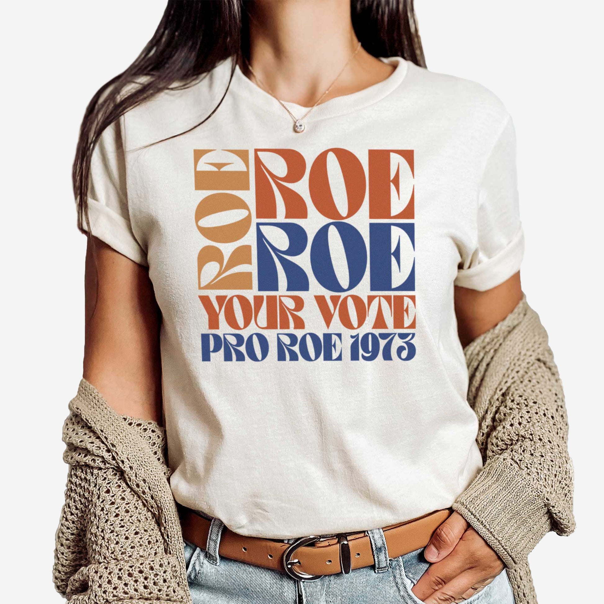 A woman wearing a soft cream Bella Canvas t-shirt featuring the words roe roe roe your vote pro roe 1973 in a retro font.