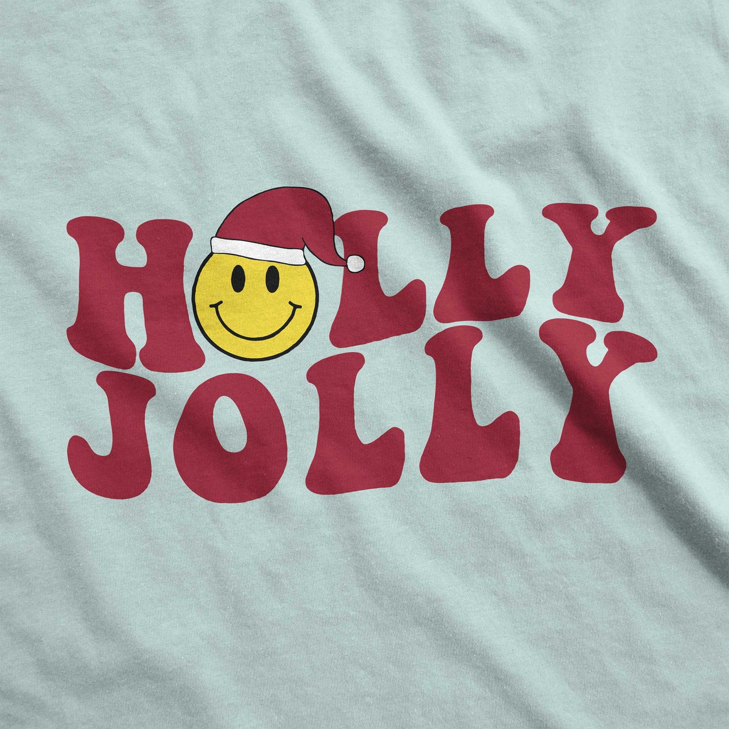 A dusty blue Bella Canvas swatch featuring a yellow smiley face with a santa hat among the words holly jolly.