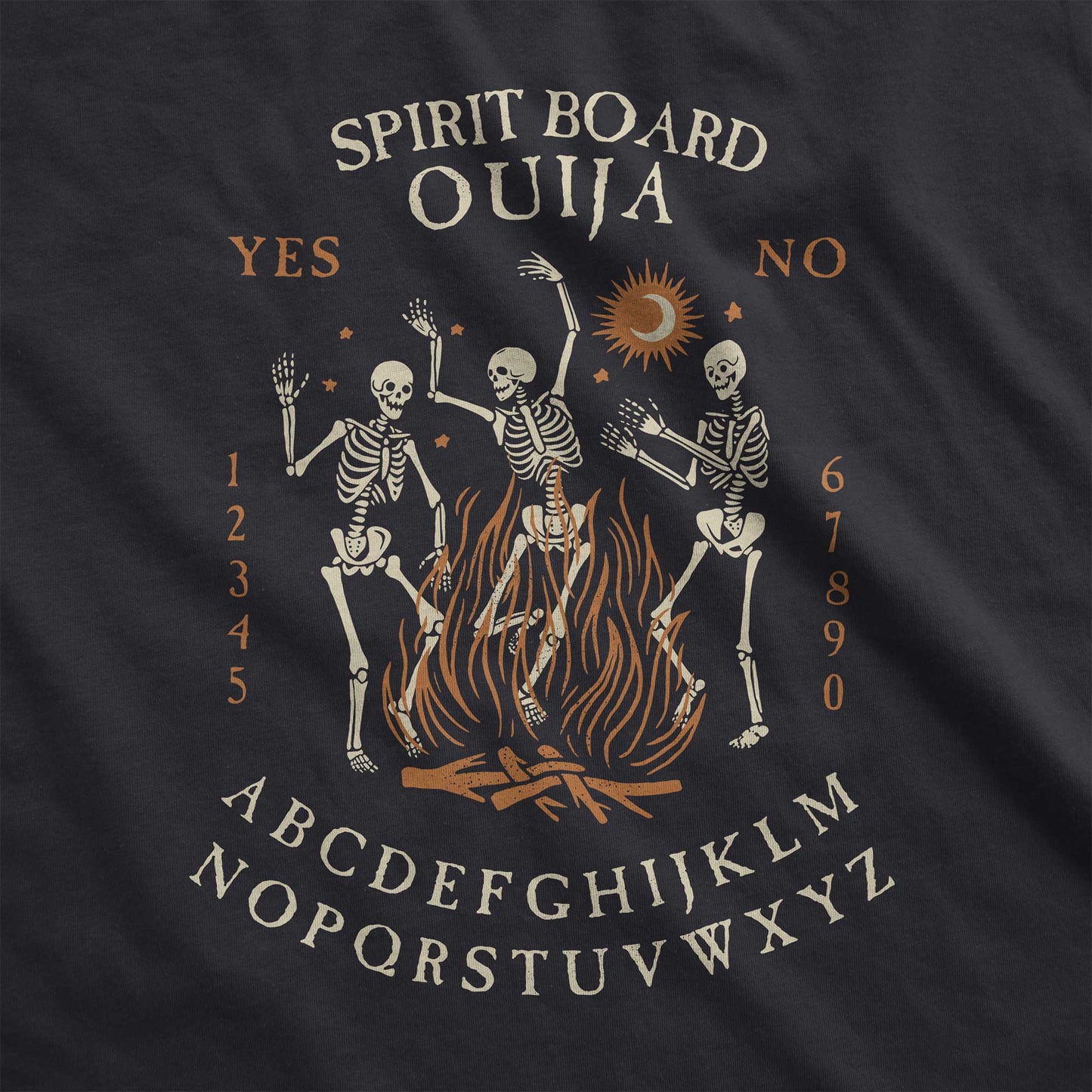 A black Bella Canvas swatch with dancing skeletons in front of a fire and an ouija board layout.