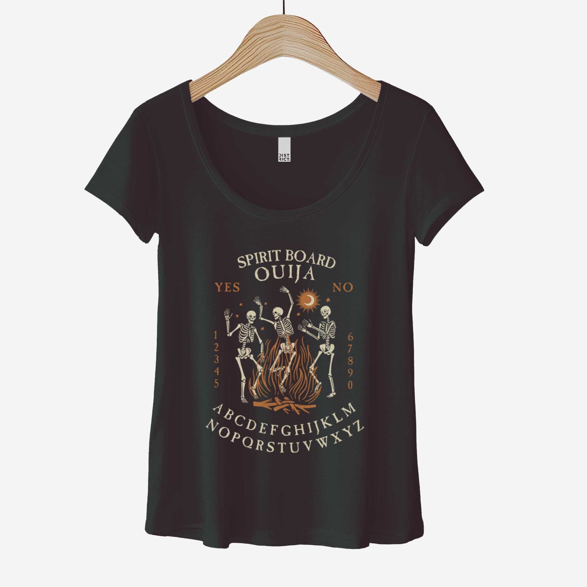 A hanging black District 7501 scoop neck t-shirt featuring dancing skeletons in front of a fire and an ouija board layout.