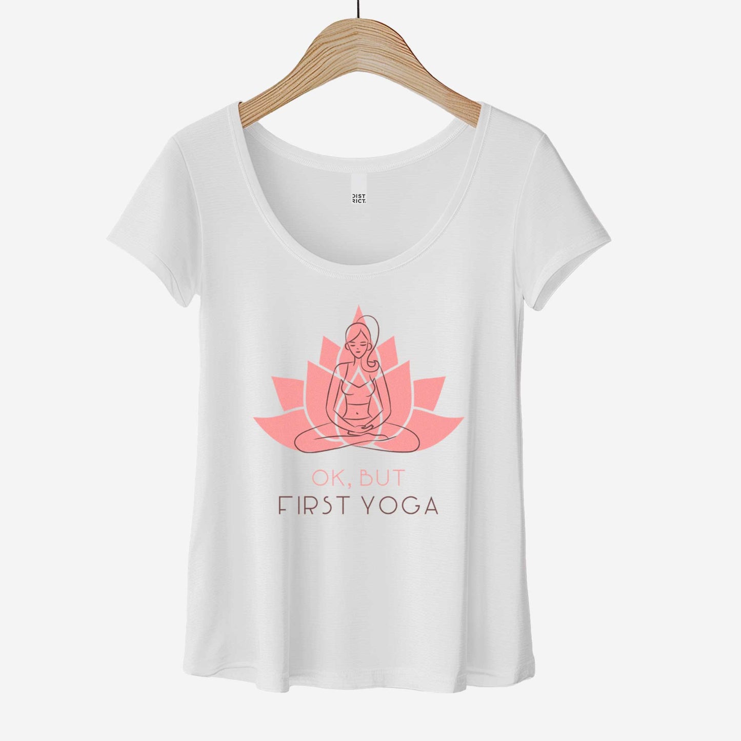 A hanging white District 7501 scoop neck t-shirt featuring a woman in the yoga lotus pose overlayed on top of a lotus flower and the words ok but first yoga.