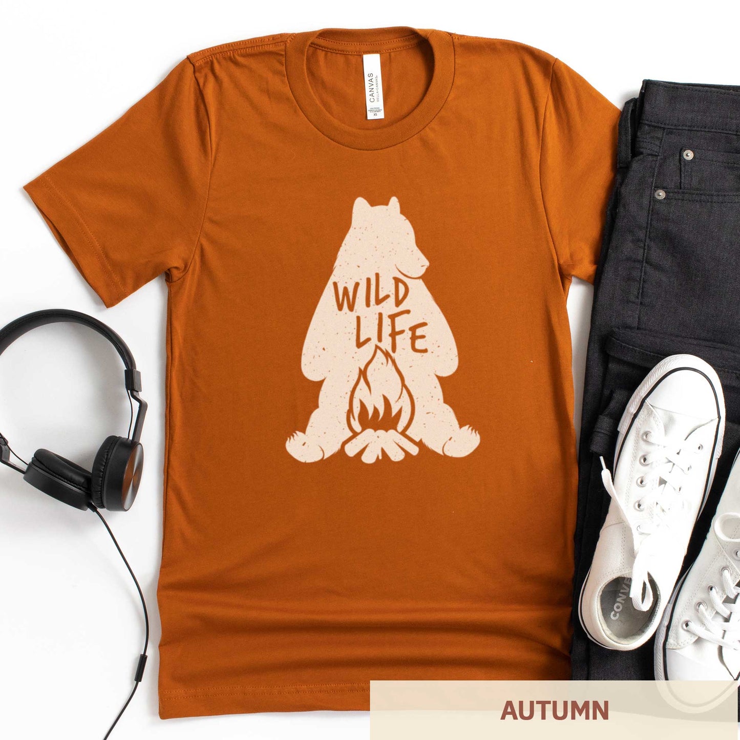 An autumn burnt orange Bella Canvas t-shirt featuring a silhouette of a grizzly bear sitting in front of a campfire with the words wild life.