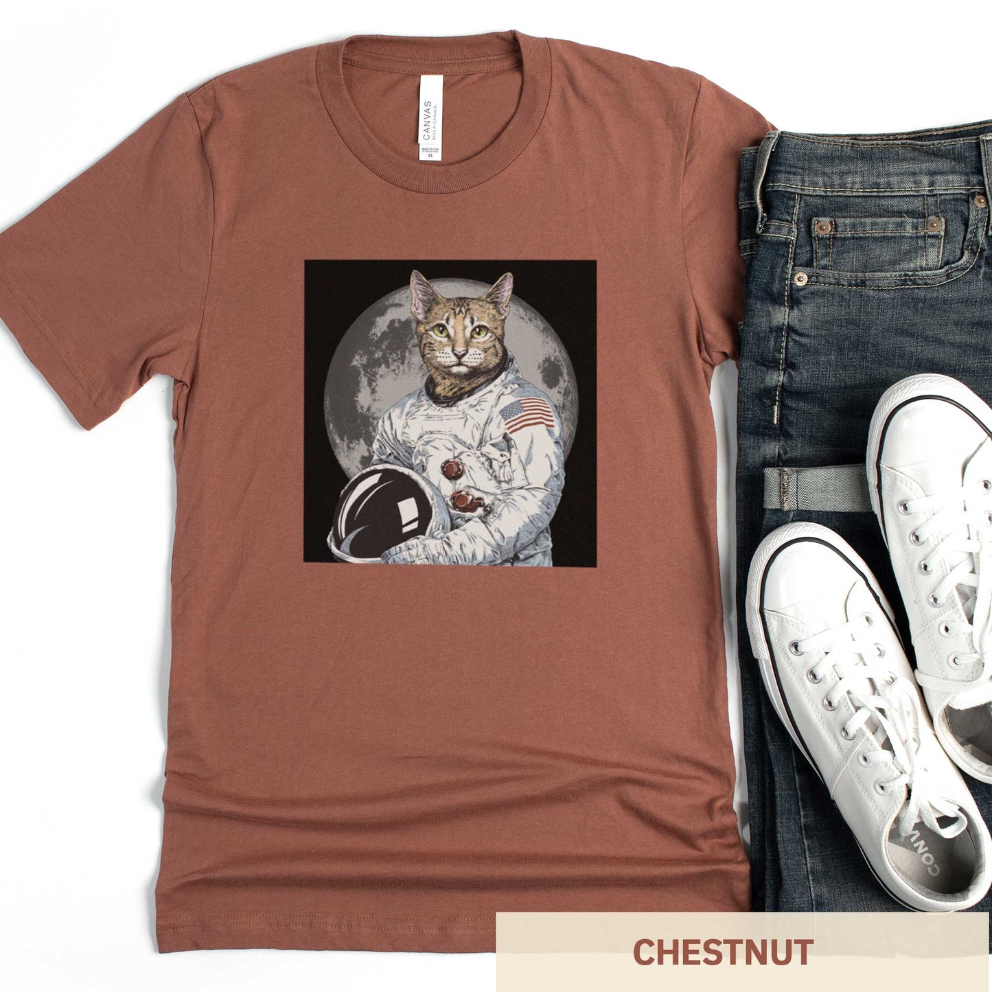 A chestnut cocoa brown Bella Canvas t-shirt featuring an illustrated portrait of a cat as a NASA astronaut with the moon in the background.