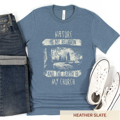 A heather slate Bella Canvas t-shirt featuring fields and a forest with the words nature is my religion and the earth is my church.