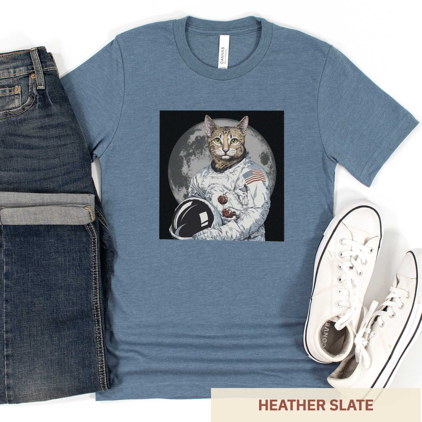 A heather slate Bella Canvas t-shirt featuring an illustrated portrait of a cat as a NASA astronaut with the moon in the background.