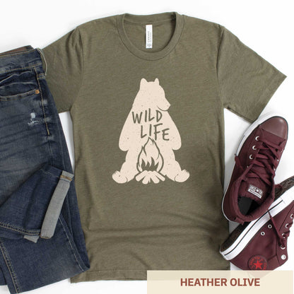 A heather olive Bella Canvas t-shirt featuring a silhouette of a grizzly bear sitting in front of a campfire with the words wild life.
