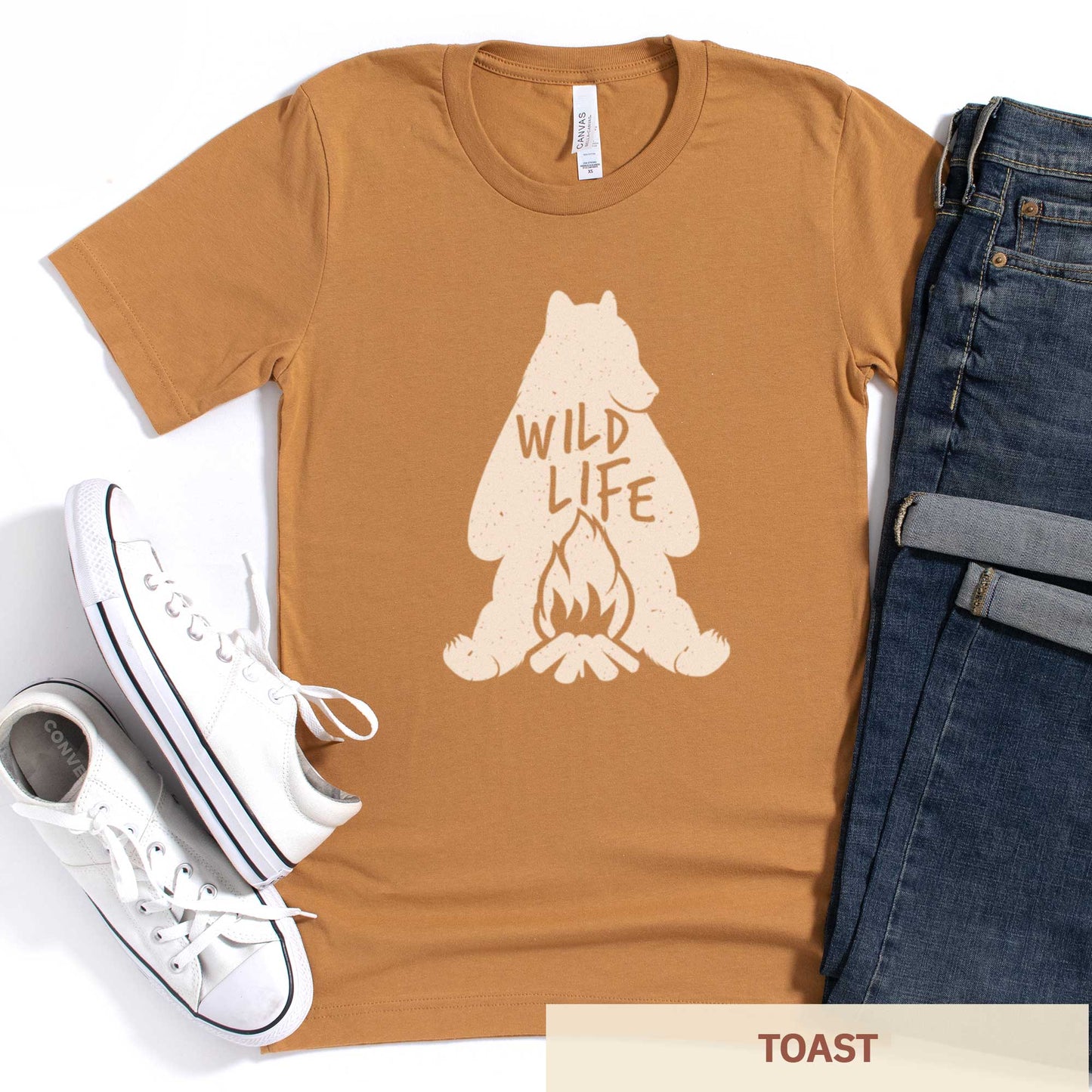 A toast brownish yellow Bella Canvas t-shirt featuring a silhouette of a grizzly bear sitting in front of a campfire with the words wild life.