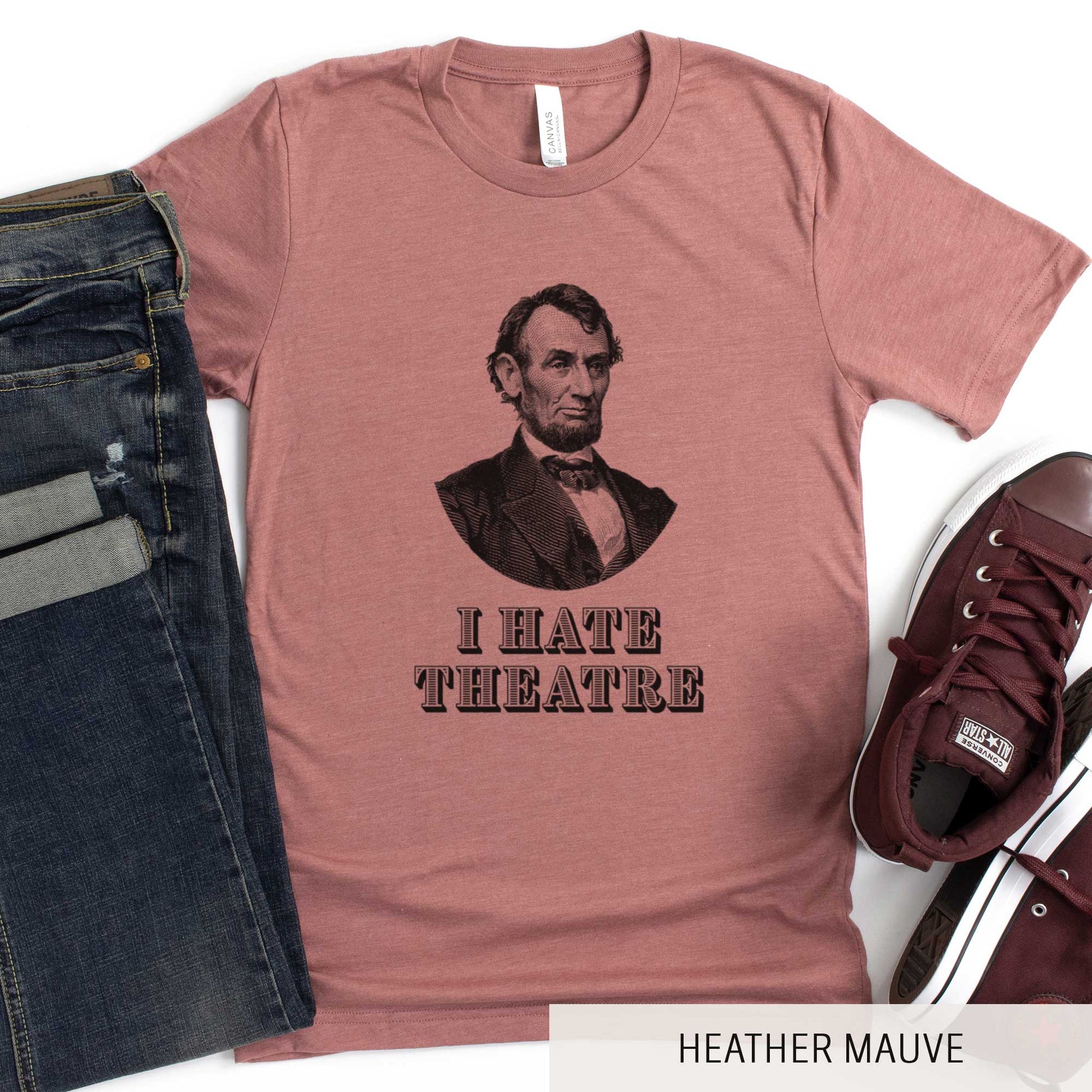 A heather mauve Bella Canvas t-shirt featuring a vintage illustration of Abraham Lincoln with the words I hate theatre below it.