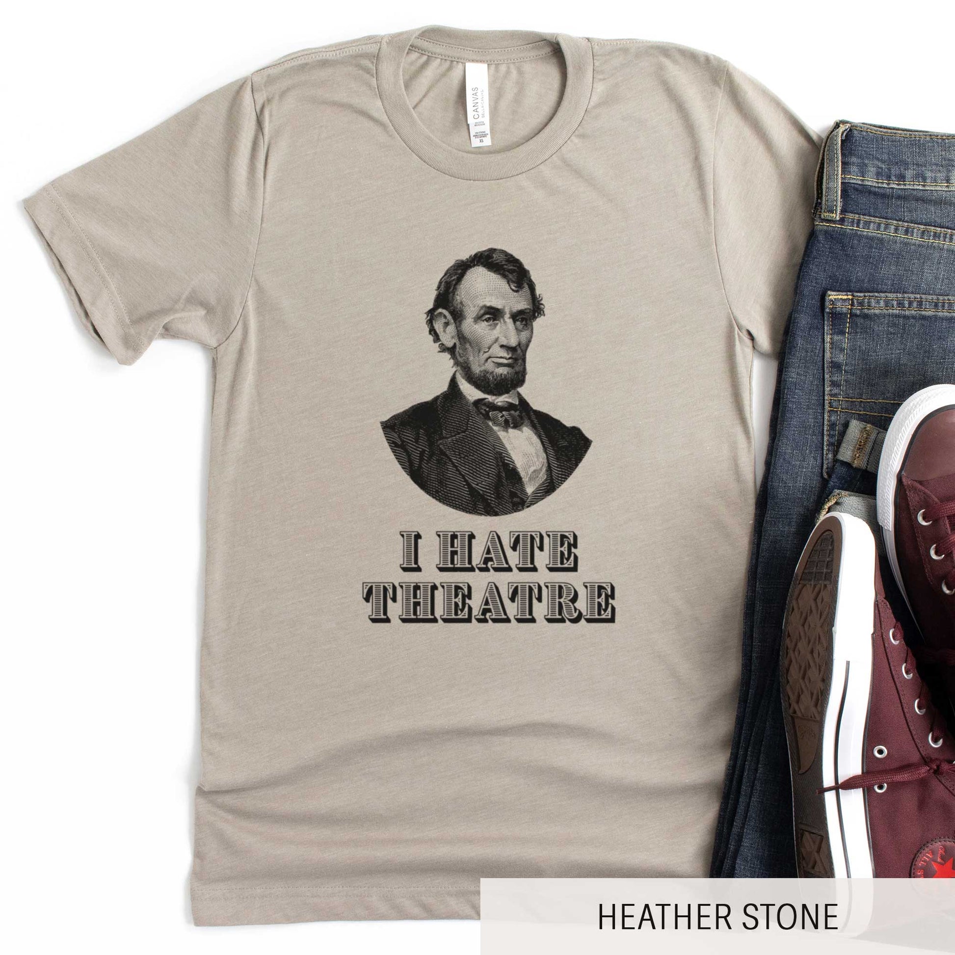 A heather stone Bella Canvas t-shirt featuring a vintage illustration of Abraham Lincoln with the words I hate theatre below it.