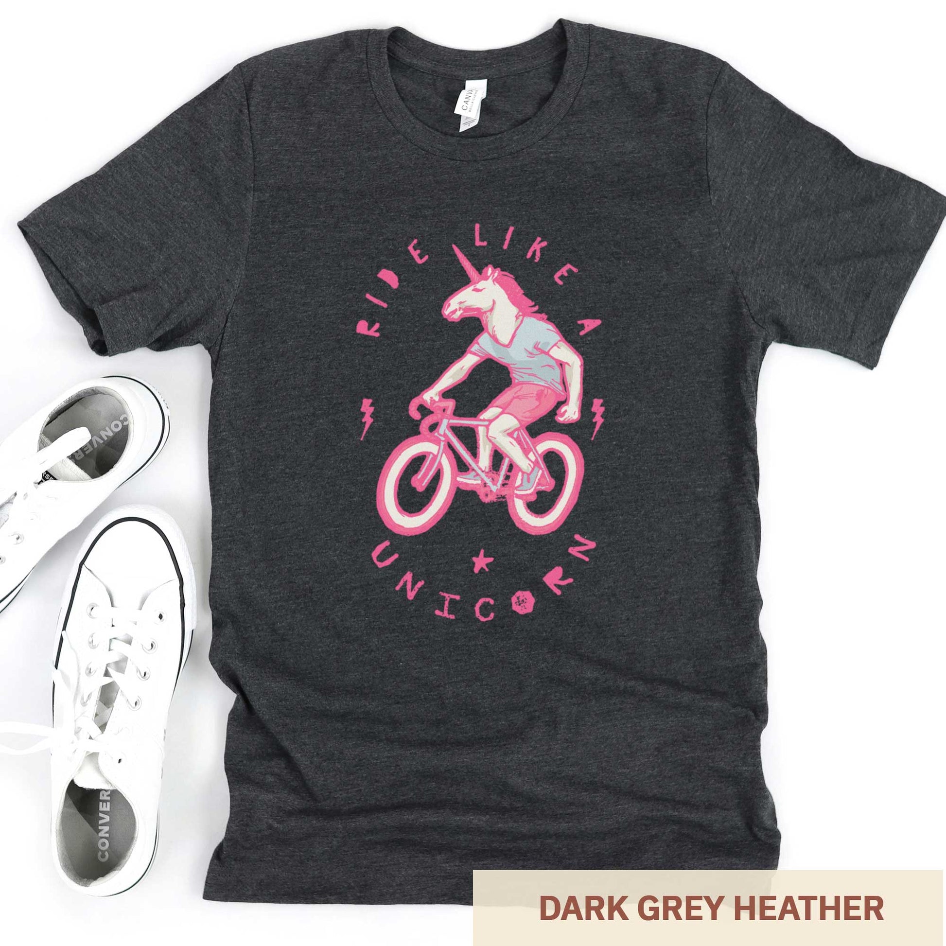 A dark grey heather Bella Canvas t-shirt featuring a neon pink unicorn riding a bike and the words ride like a unicorn.