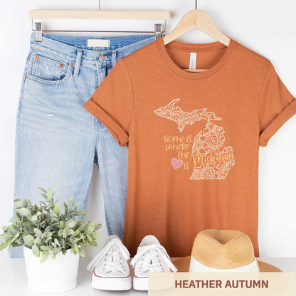 A hanging heather autumn Bella Canvas t-shirt featuring a mandala in the shape of Michigan with the words home is where the heart is.
