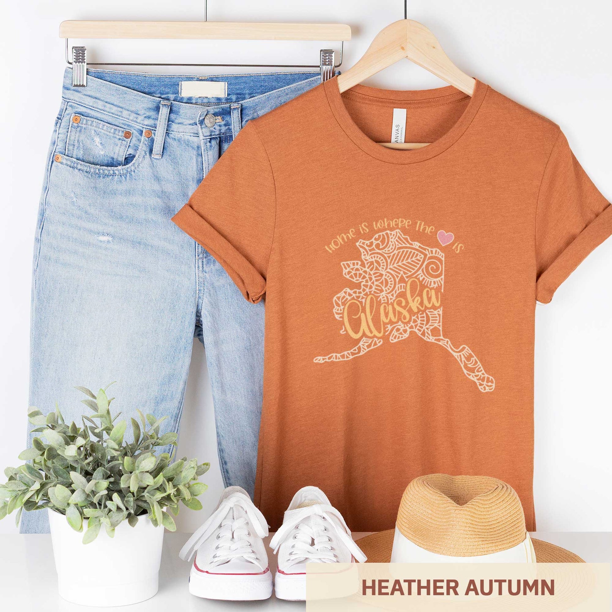 A hanging heather autumn Bella Canvas t-shirt featuring a mandala in the shape of Alaska with the words home is where the heart is.