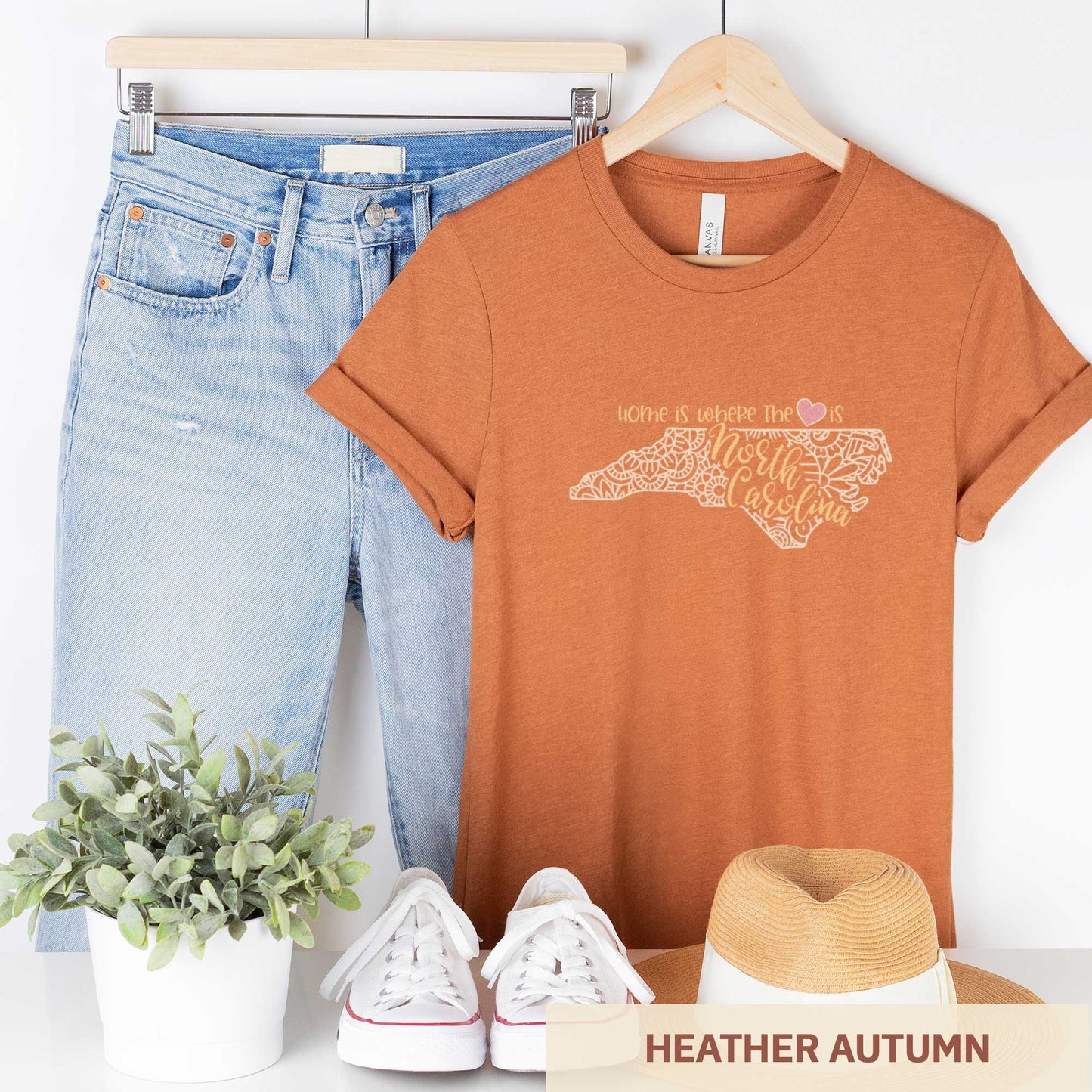 A hanging heather autumn Bella Canvas t-shirt featuring a mandala in the shape of North Carolina with the words home is where the heart is.