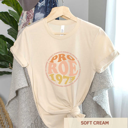 A hanging soft cream Bella Canvas t-shirt featuring the words pro roe 1973 in retro font.