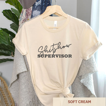 A hanging soft cream Bella Canvas t-shirt featuring the text shitshow supervisor.