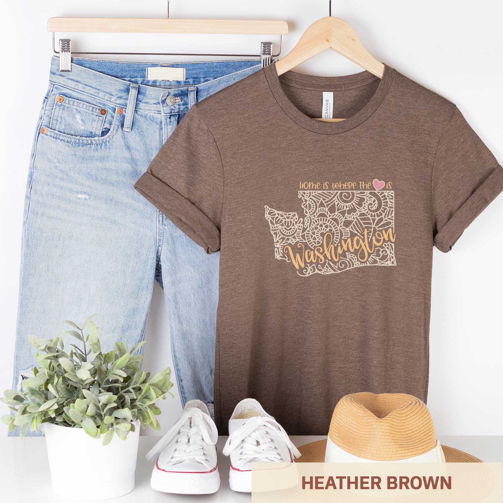 A hanging heather brown Bella Canvas t-shirt featuring a mandala in the shape of Washington with the words home is where the heart is.