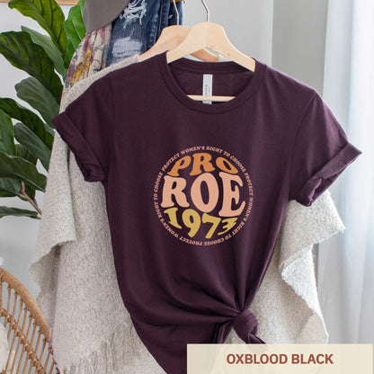 A hanging oxblood black Bella Canvas t-shirt featuring the words pro roe 1973 in retro font.
