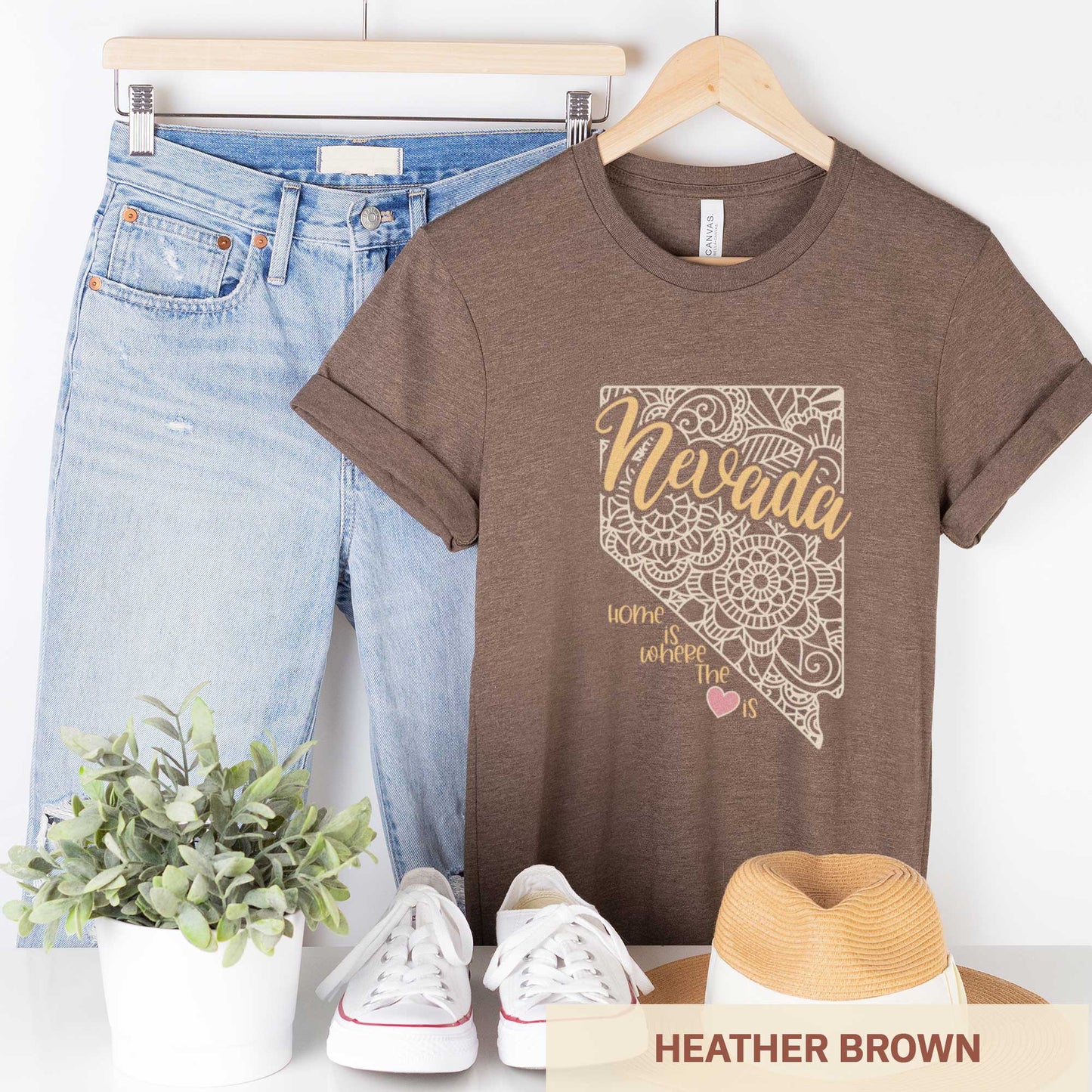 A hanging heather brown Bella Canvas t-shirt featuring a mandala in the shape of Nevada with the words home is where the heart is.