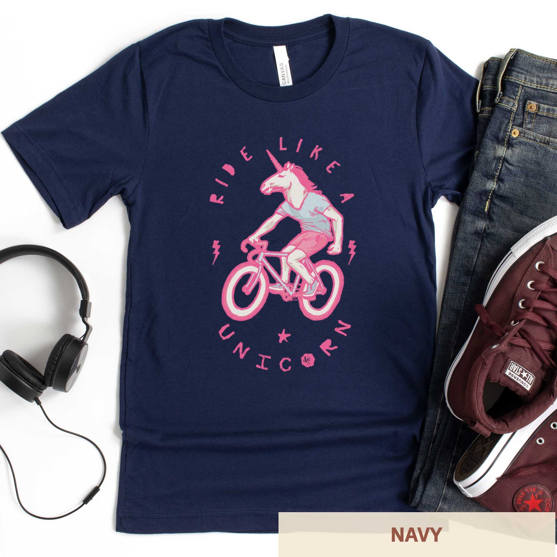 A navy Bella Canvas t-shirt featuring a neon pink unicorn riding a bike and the words ride like a unicorn.