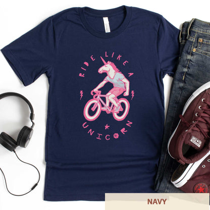 A navy Bella Canvas t-shirt featuring a neon pink unicorn riding a bike and the words ride like a unicorn.