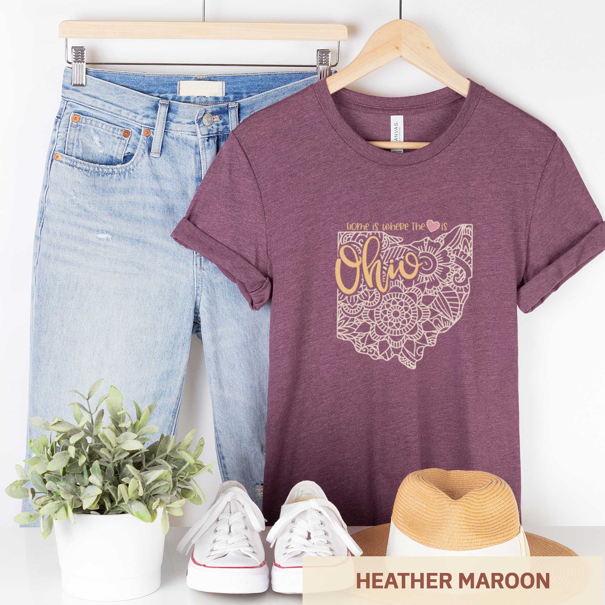 A hanging heather maroon Bella Canvas t-shirt featuring a mandala in the shape of Ohio with the words home is where the heart is.