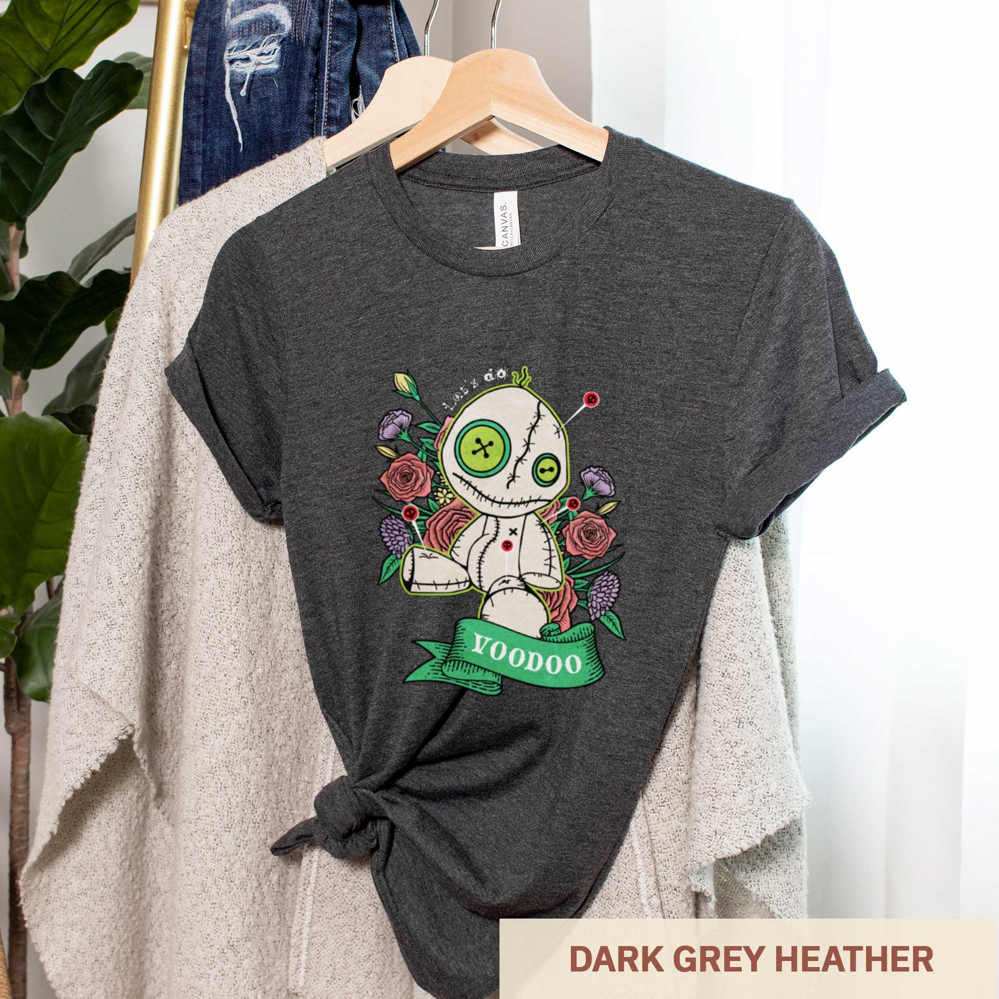 A dark grey heather Bella Canvas t-shirt featuring a cartoon voodoo doll and flowers.