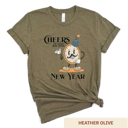 A heather olive Bella Canvas t-shirt featuring a retro looking clock cartoon with a party hat next to the words Cheers to the New Year.
