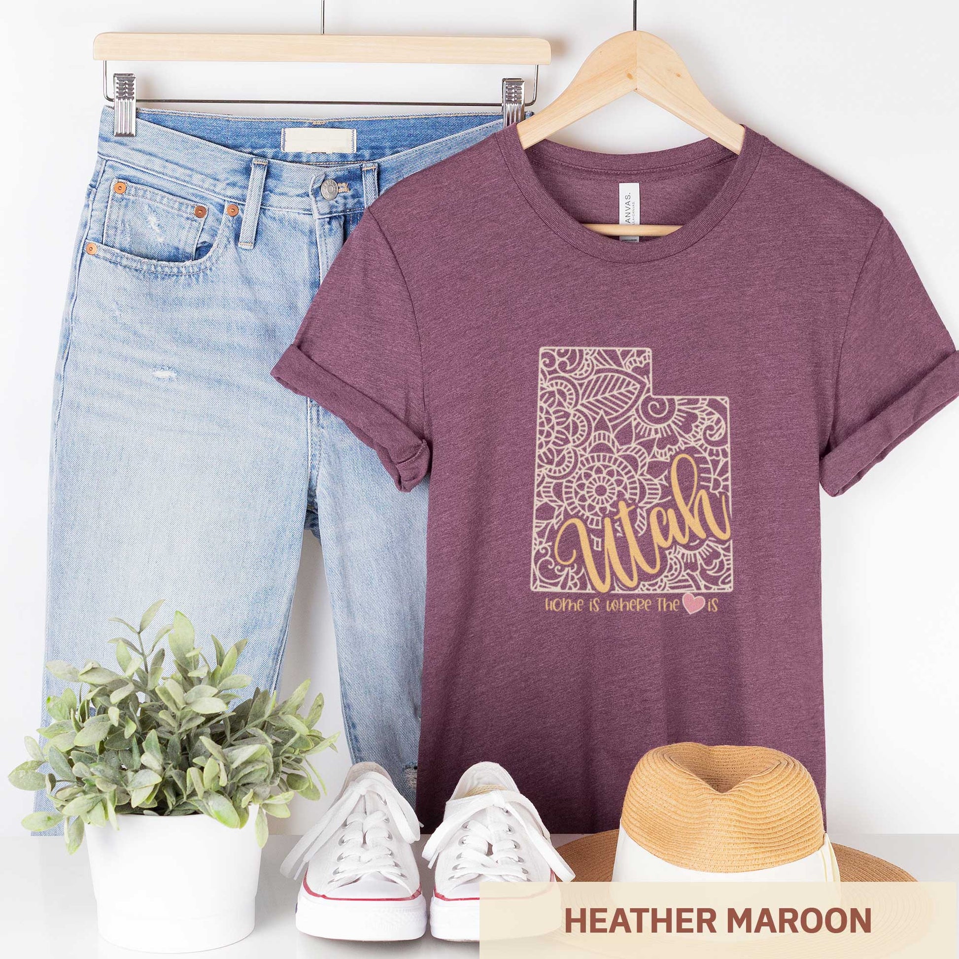A hanging heather maroon Bella Canvas t-shirt featuring a mandala in the shape of Utah with the words home is where the heart is.