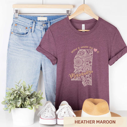 A hanging heather maroon Bella Canvas t-shirt featuring a mandala in the shape of Mississippi with the words home is where the heart is.