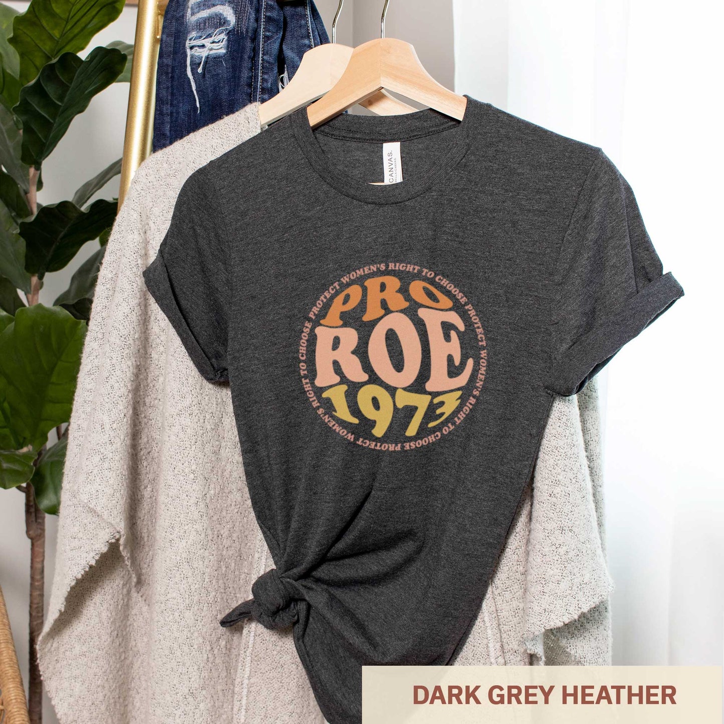 A hanging dark grey heather Bella Canvas t-shirt featuring the words pro roe 1973 in retro font.