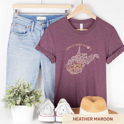 A hanging heather maroon Bella Canvas t-shirt featuring a mandala in the shape of West Virginia with the words home is where the heart is.