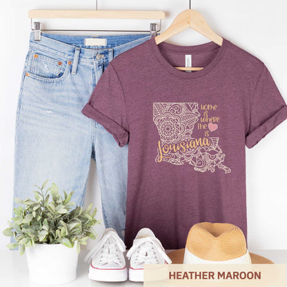 A hanging heather maroon Bella Canvas t-shirt featuring a mandala in the shape of Louisiana with the words home is where the heart is.