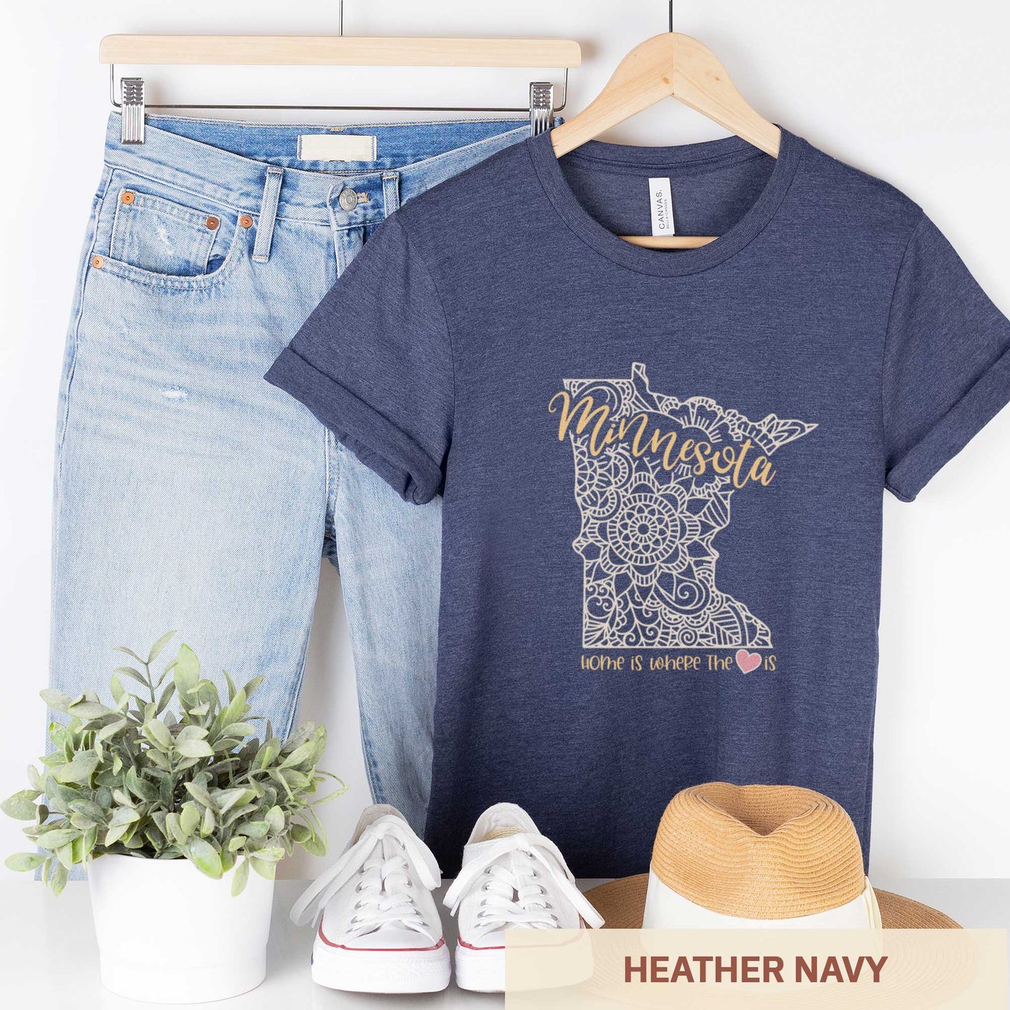 A hanging heather navy Bella Canvas t-shirt featuring a mandala in the shape of Minnesota with the words home is where the heart is.