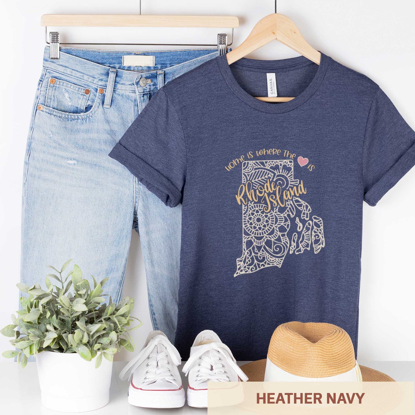A hanging heather navy Bella Canvas t-shirt featuring a mandala in the shape of Rhode Island with the words home is where the heart is.