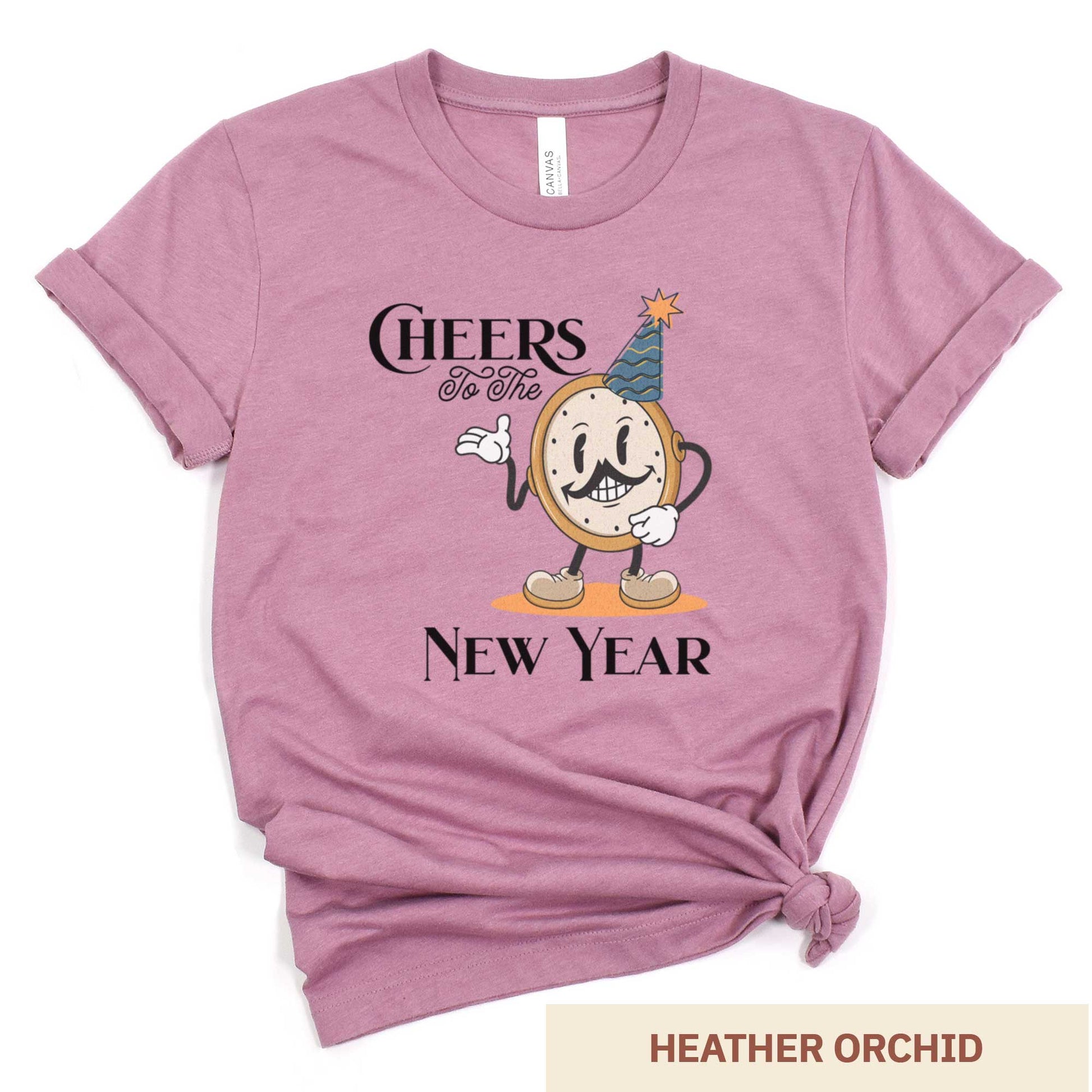 A heather orchid Bella Canvas t-shirt featuring a retro looking clock cartoon with a party hat next to the words Cheers to the New Year.