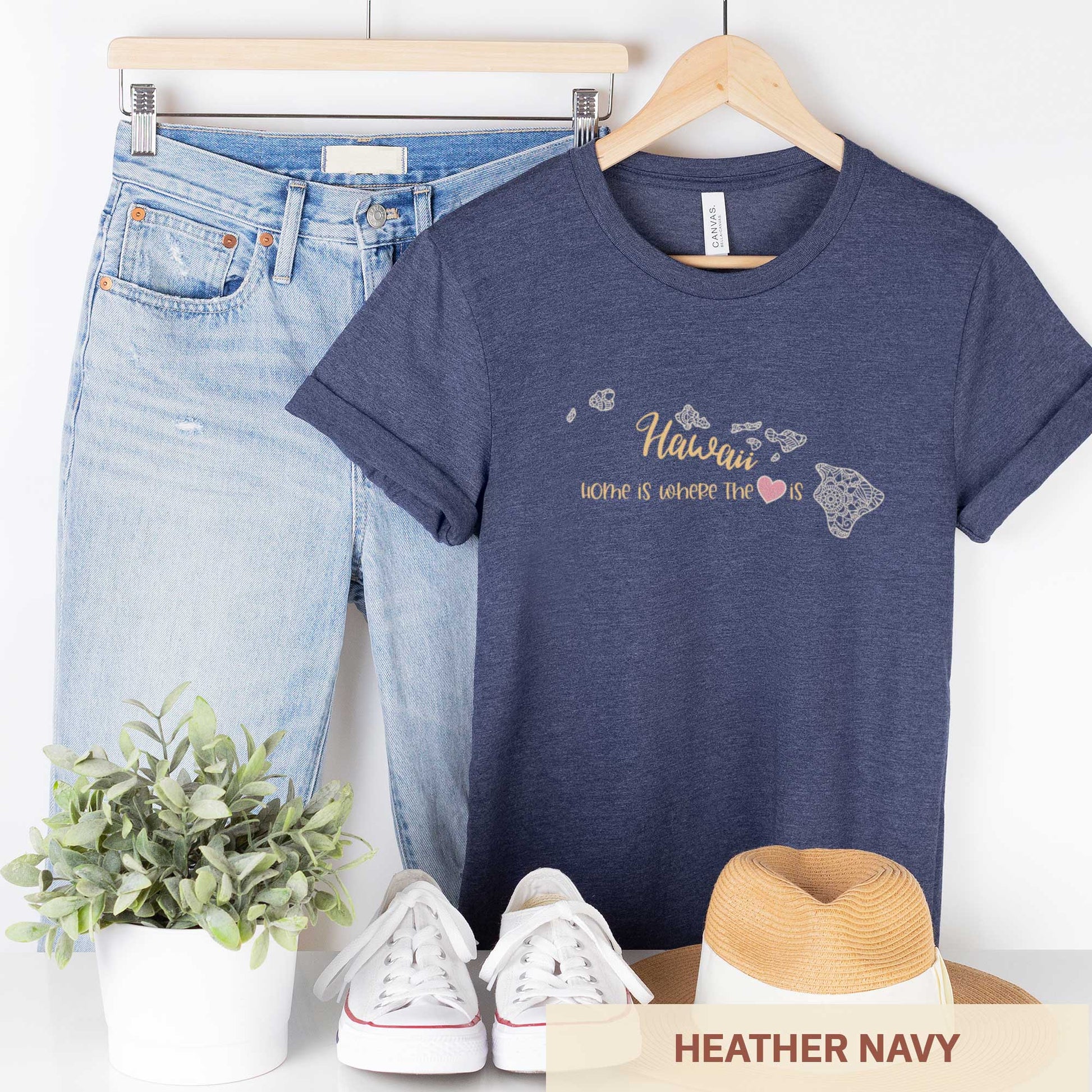 A hanging heather navy Bella Canvas t-shirt featuring a mandala in the shape of Hawaii with the words home is where the heart is.