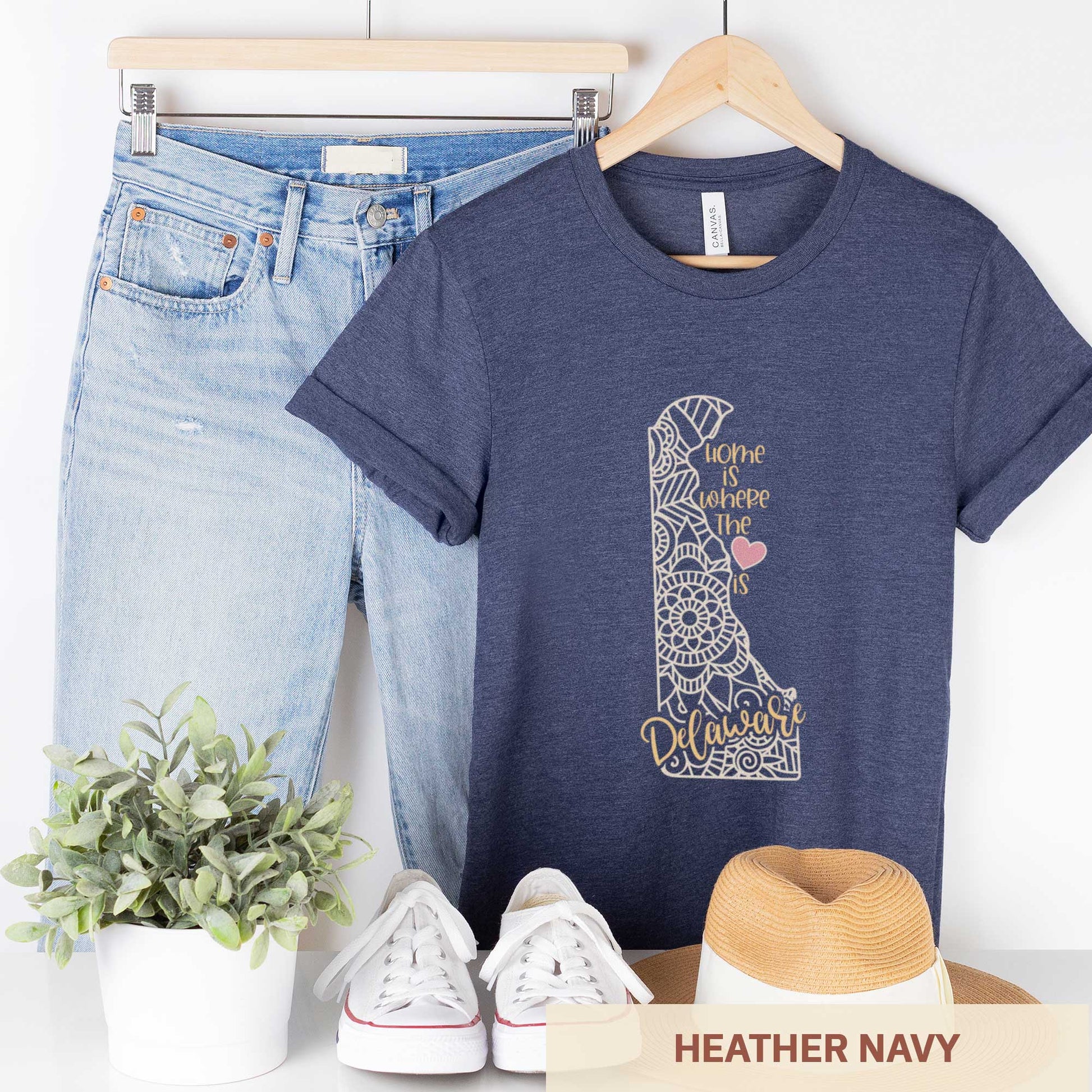 A hanging heather navy Bella Canvas t-shirt featuring a mandala in the shape of Delaware with the words home is where the heart is.