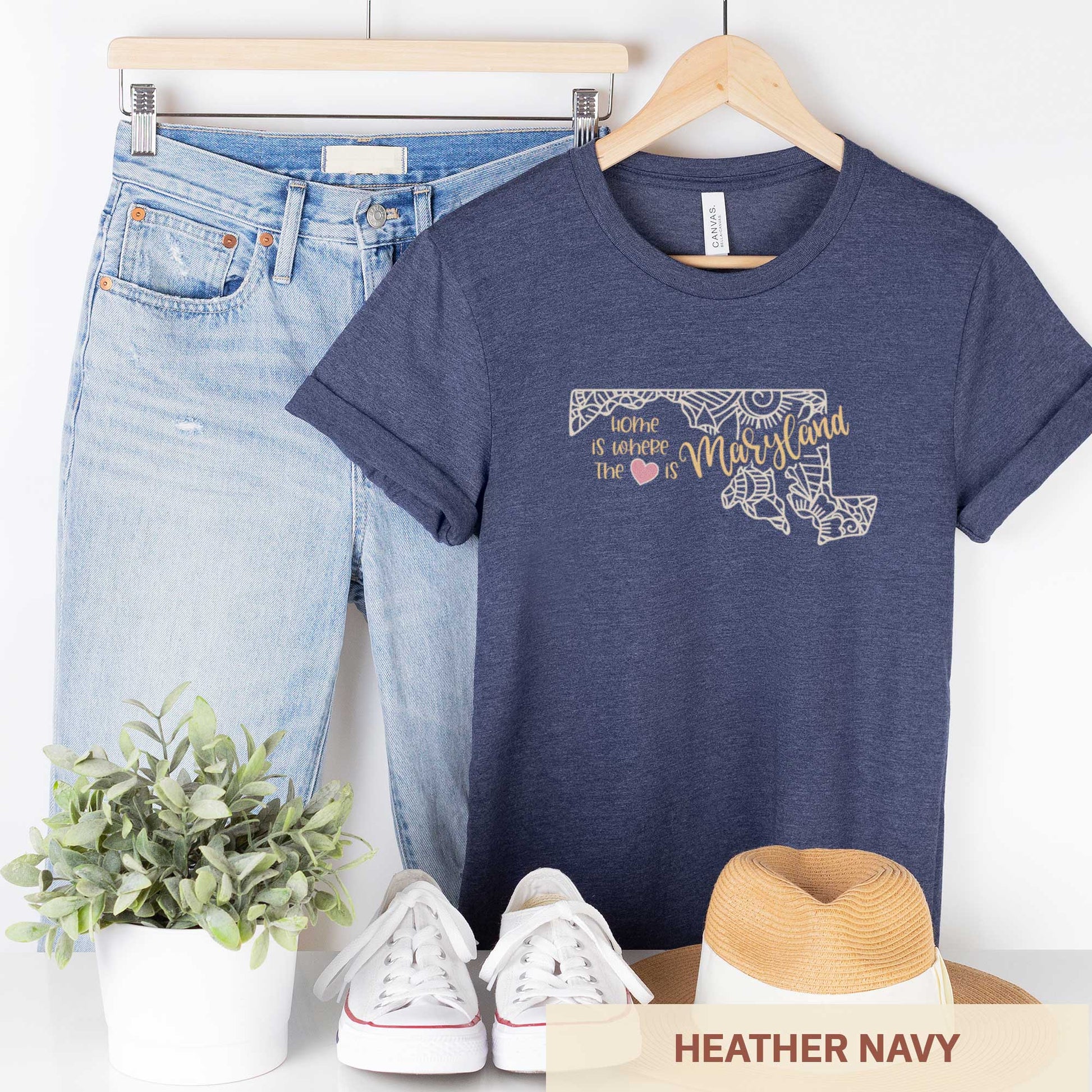 A hanging heather navy Bella Canvas t-shirt featuring a mandala in the shape of Maryland with the words home is where the heart is.