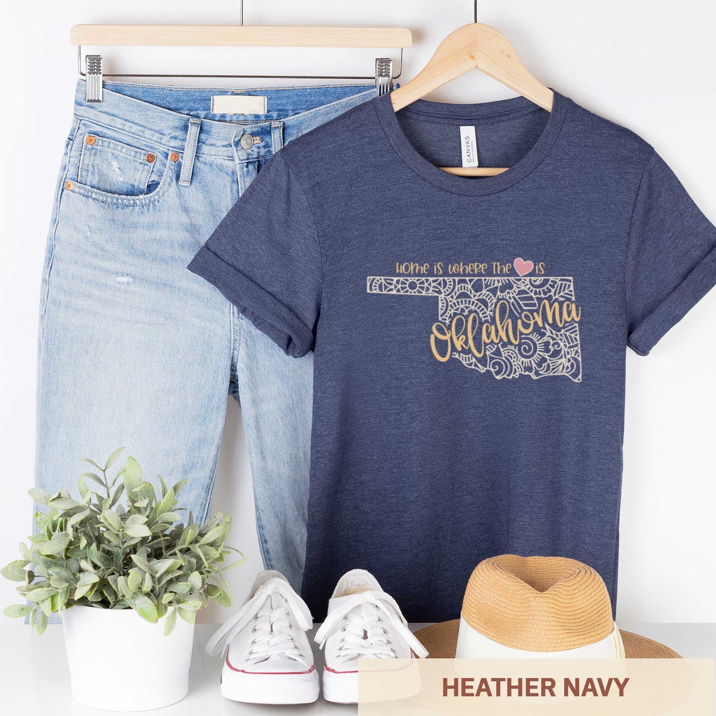 A hanging heather navy Bella Canvas t-shirt featuring a mandala in the shape of Oklahoma with the words home is where the heart is.