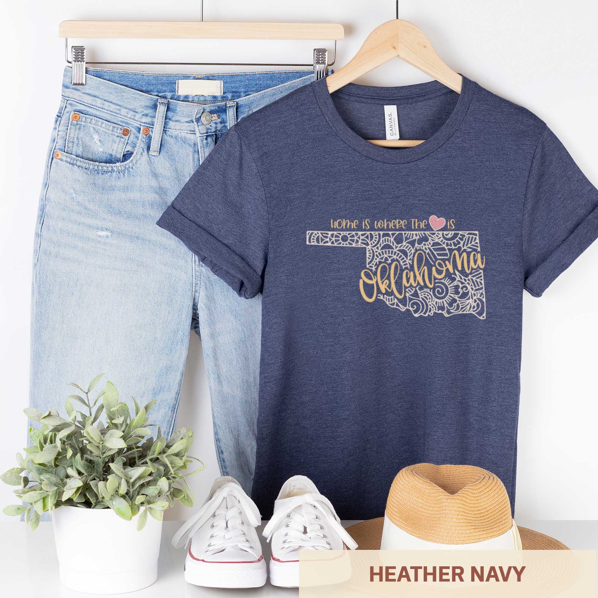 A hanging heather navy Bella Canvas t-shirt featuring a mandala in the shape of Oklahoma with the words home is where the heart is.