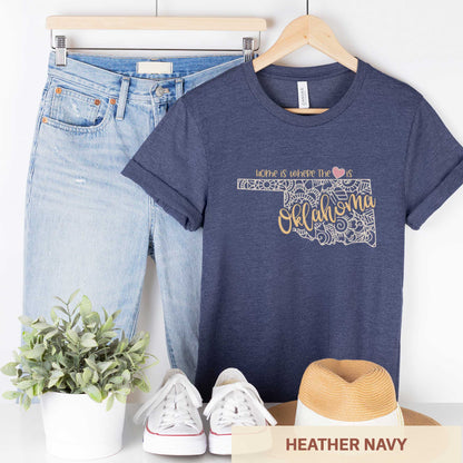 A hanging heather navy Bella Canvas t-shirt featuring a mandala in the shape of Oklahoma with the words home is where the heart is.