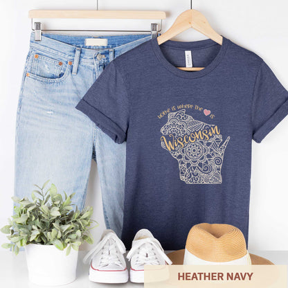 A hanging heather navy Bella Canvas t-shirt featuring a mandala in the shape of Wisconsin with the words home is where the heart is.