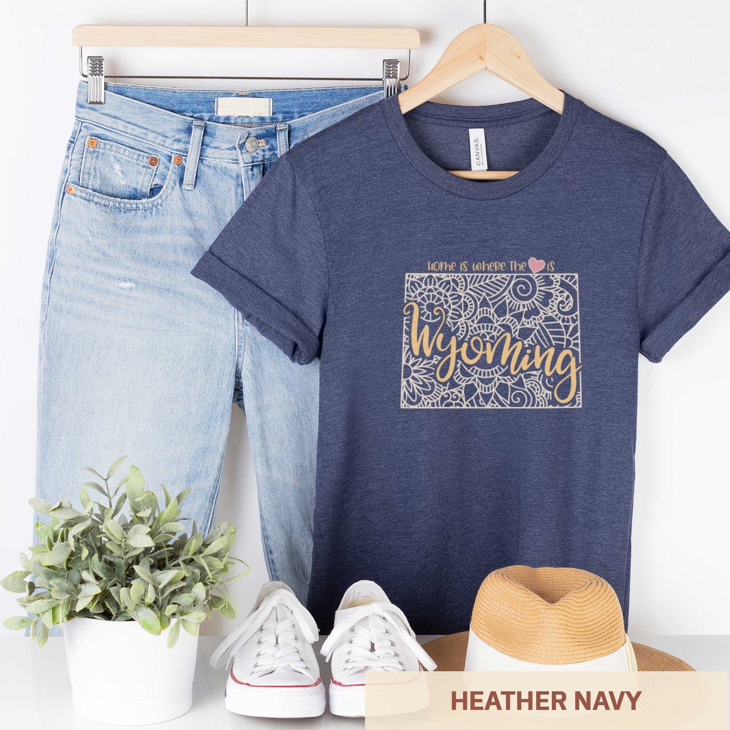 A hanging heather navy Bella Canvas t-shirt featuring a mandala in the shape of Wyoming with the words home is where the heart is.