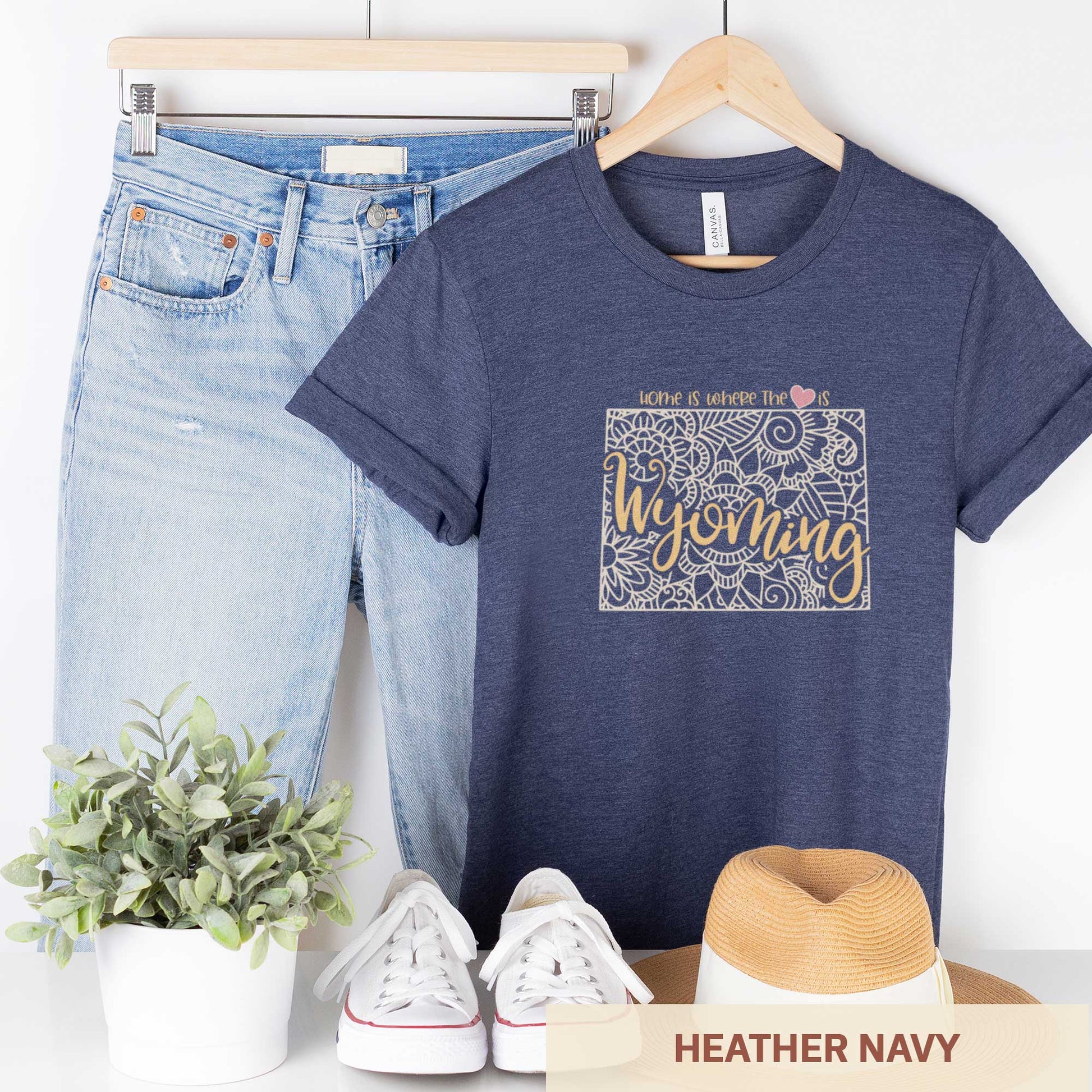 A hanging heather navy Bella Canvas t-shirt featuring a mandala in the shape of Wyoming with the words home is where the heart is.