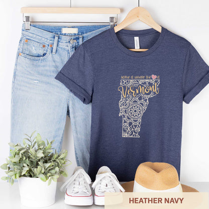 A hanging heather navy Bella Canvas t-shirt featuring a mandala in the shape of Vermont with the words home is where the heart is.