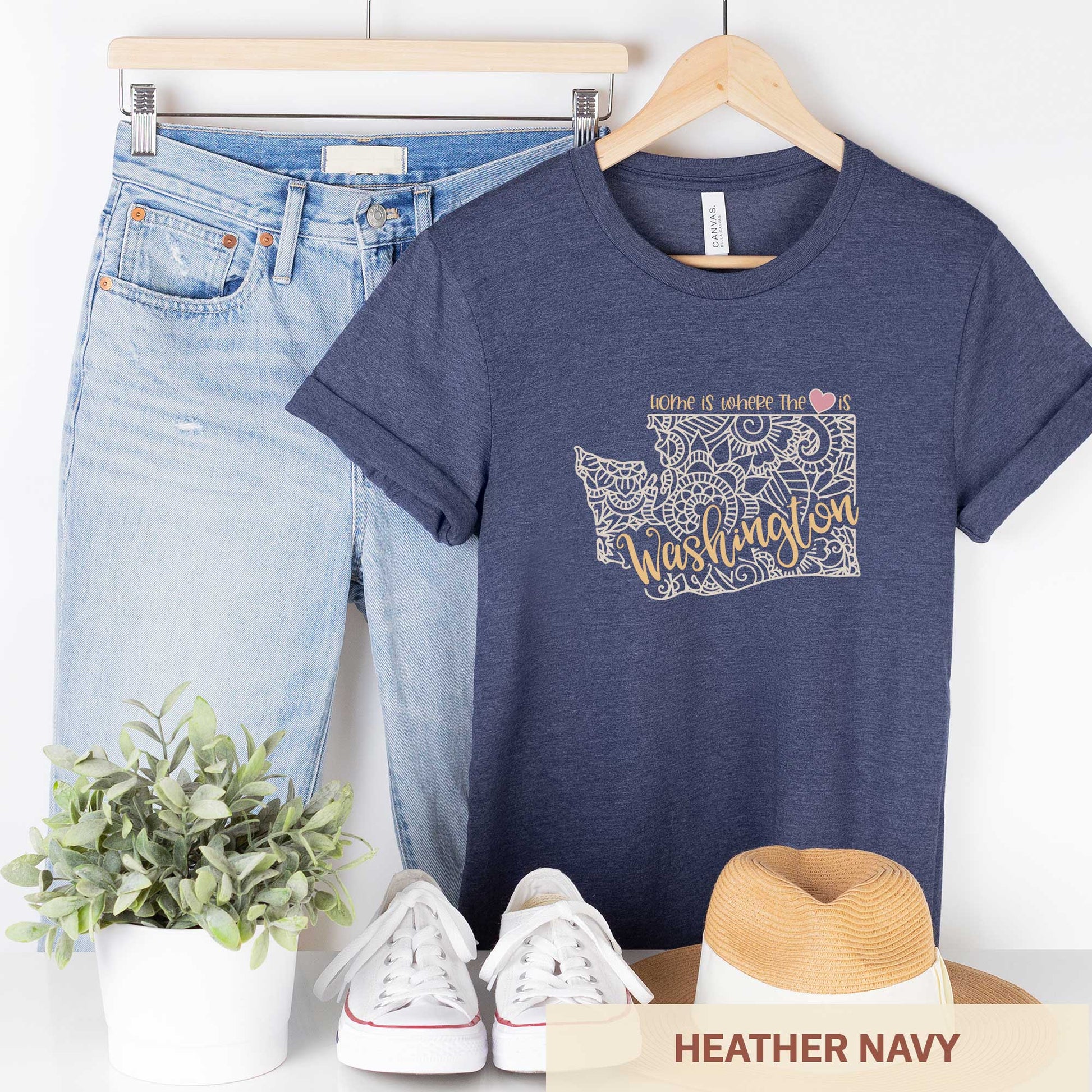 A hanging heather navy Bella Canvas t-shirt featuring a mandala in the shape of Washington with the words home is where the heart is.