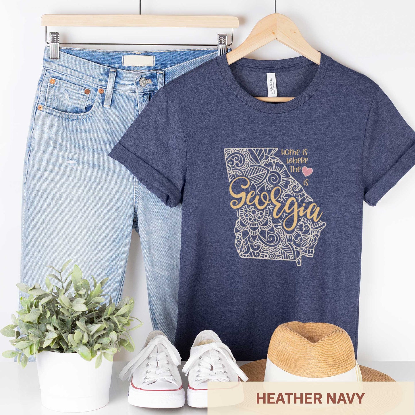 A hanging heather navy Bella Canvas t-shirt featuring a mandala in the shape of Georgia with the words home is where the heart is.
